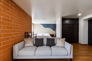 Un salon moderne avec un canapé, un mur en briques et un lit à l’arrière-plan.
