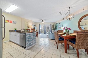 A modern kitchen with a built-in island, dining area with wicker chairs, and a large mirror on the wall. - Tradewinds 306 | Indoor, Outdoor Pools | Beachfront | My Beach Getaways (Orange Beach)