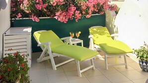 Um pátio com duas cadeiras de descanso brancas e uma mesa pequena com bebidas.