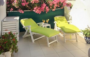Eine Terrasse mit zwei weißen Liegestühlen und einem kleinen Tisch mit Getränken.