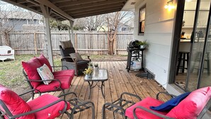A covered patio with red cushioned chairs, a small table, and a grill cart. - Kechi Kottage- Sept. special- 20% off 2+ ni stay! Ask host. Pet friendly. Safe! (Kechi)