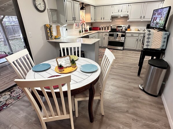 A modern kitchen with white cabinets, a central island, and a dining area with white chairs.