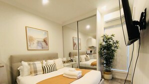 Une chambre d’hôtel avec un grand lit, un téléviseur à écran plat fixé au mur, une plante en pot et une fenêtre donnant sur un beau paysage.