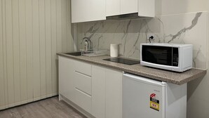 Une cuisine compacte avec des meubles blancs, un pare-feu en marbre, un four à micro-ondes encastré et un évier doté d’un distributeur de savon.