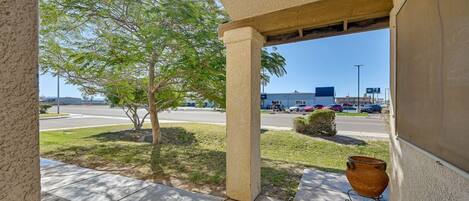 A building entrance with a concrete pillar, a potted plant, and a view of a parking lot and road.