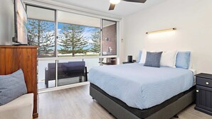 A bedroom with a large bed, a ceiling fan, a sliding glass door leading to a balcony, and a nightstand with a lamp. - Reddall Waterside Stay (Lake Illawarra)