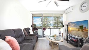 A modern living room with a grey sofa, a glass coffee table, and a television on a stand. - Reddall Waterside Stay (Lake Illawarra)