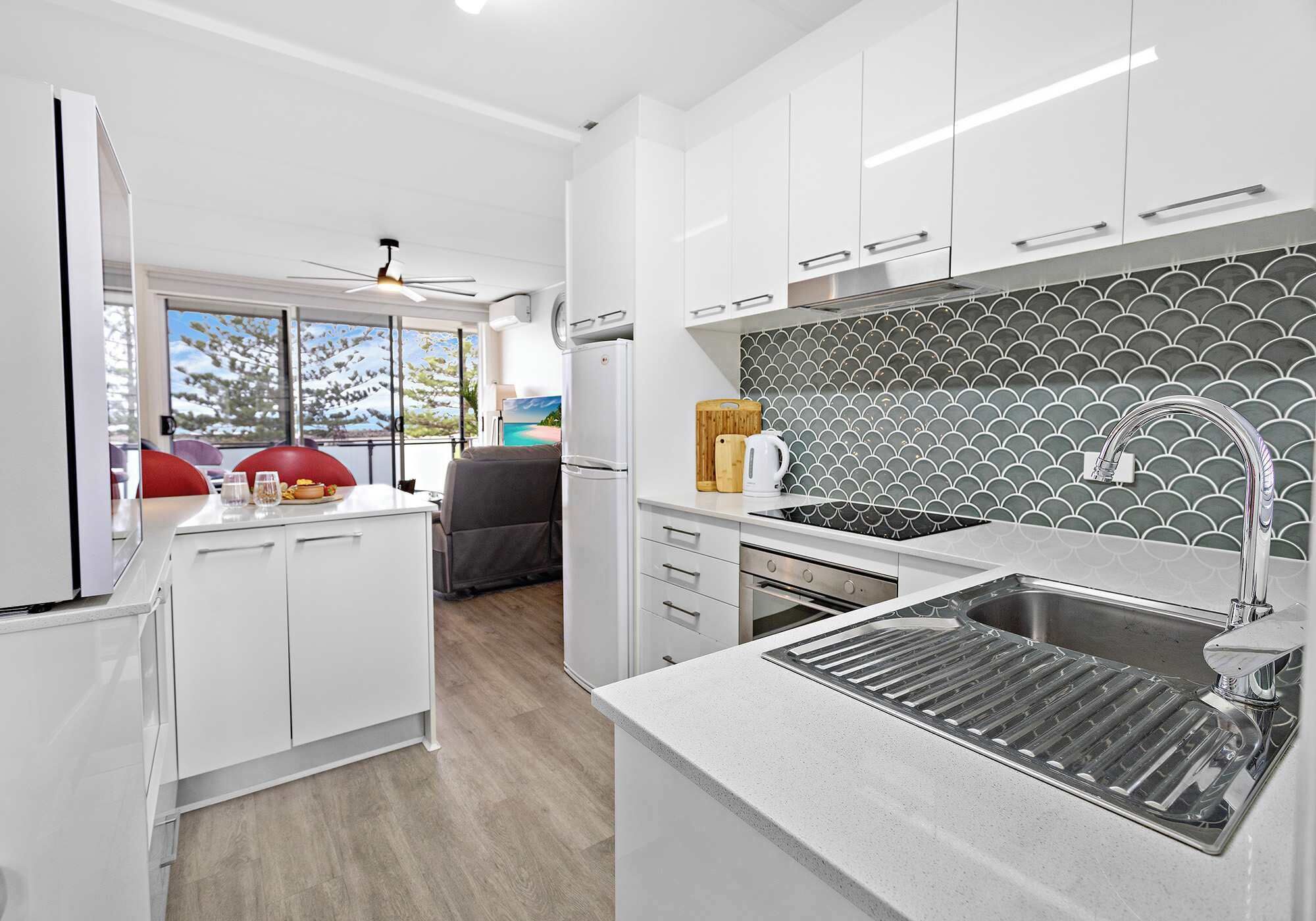 A modern kitchen with white cabinets, a stainless steel sink, and a patterned backsplash.