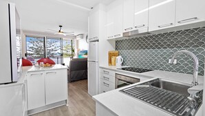 A modern kitchen with white cabinets, a stainless steel sink, and a patterned backsplash. - Reddall Waterside Stay (Lake Illawarra)