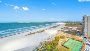 Vista sulla costa con spiaggia, oceano e campo da tennis adiacente a un grattacielo.