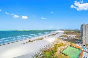 Blick auf die Küste mit Strand, Meer und einem Tennisplatz neben einem Hochhaus.