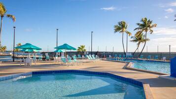 A pool area with multiple lounge chairs and umbrellas, surrounded by palm trees.