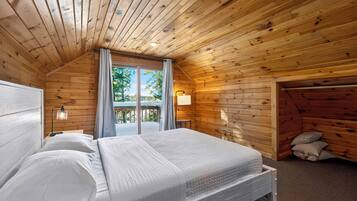 Une chambre à coucher dans une cabane en bois, avec un lit, deux lampes de chevet, une fenêtre avec des rideaux et une vue sur l’extérieur.