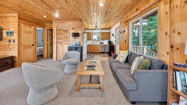 A wooden cabin interior with a living room, sofa, armchair, coffee table, kitchen, and large windows. - Cozy Pines on Diamond Lake (Cable)