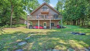 A two-story wooden cabin with a balcony, surrounded by a forested area. - Cozy Pines on Diamond Lake (Cable)