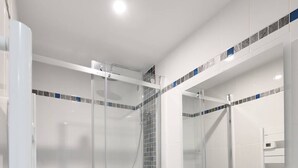 Ein modernes Badezimmer mit einer Duschkabine aus Glas, einem weißen Waschtisch mit Spiegel und einem gefliesten Boden.