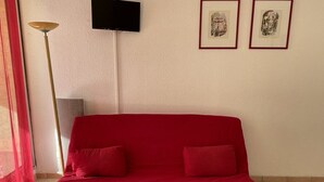 Een rode bank in een kamer met een aan de muur bevestigde televisie en twee ingekaderde foto’s erboven.