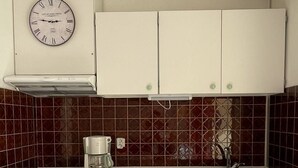 Een kleine keuken met witte kasten, een inbouwfornuis, een koffiezetapparaat en een wandklok.