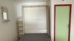 Een eenpersoonsbed met een grijze matras in een kamer met een groene deur en een witte kledingkast.
