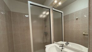 Een badkamer met een douche, wastafel en spiegel.
