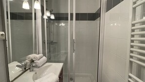 Un baño moderno con ducha separada por vidrio, un lavamanos con espejo y un perchero para toallas.