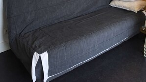 Un sofá gris con un cojín blanco y una almohada frente a una pared blanca con un diseño circular.