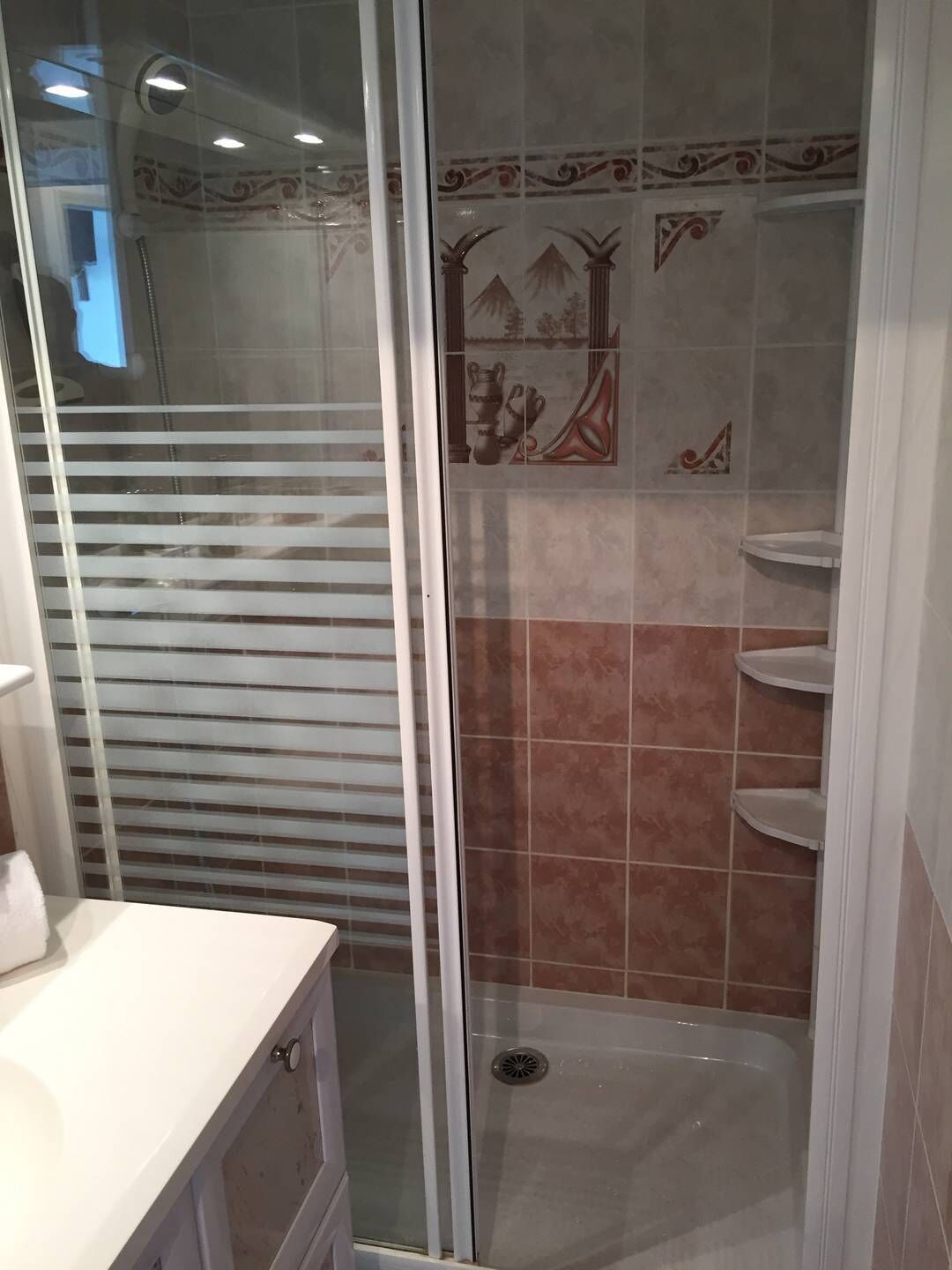 Eine Dusche mit Glastür, geflieste Wände und ein weißes Waschbecken mit Schrank.
