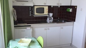 A compact kitchen with white cabinets, a microwave, a coffee maker, and a table with a green tablecloth. - Studio Héliopolis E 20 - 2 people (AGDE)