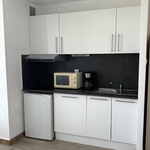 Eine kleine Küche mit weißen Schränken, einem Kühlschrank, einer Mikrowelle, einer Kaffeemaschine und einem Spülbecken.