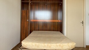 Une chambre avec une armoire en bois, un lit avec un matelas et une porte avec une horloge.