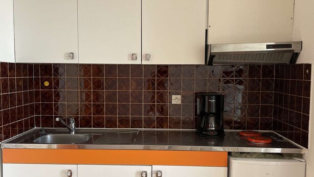Une cuisine de taille réduite avec des meubles blancs, une machine à café noire et un réfrigérateur blanc.
