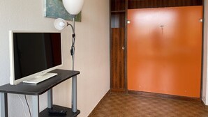Une pièce avec un téléviseur posé sur un meuble, un bureau avec une lampe et une porte orange.