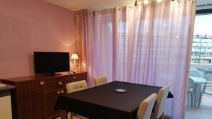 A hotel room with a dining table, chairs, a television, and a view of the outside. - Apartment Héliopolis E 78 - 4 people (AGDE)