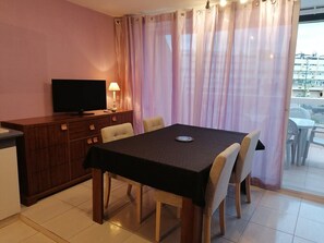A hotel room with a dining table, chairs, a television, and a view of the outside. - Apartment Héliopolis E 78 - 4 people (AGDE)