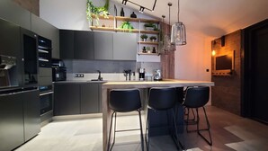 Een moderne keuken met een centraal eiland, barstoelen, inbouwapparatuur en een accentmuur van baksteen.