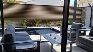 Een modern terras buiten met een zwembad, lounge fauteuils en een zitgedeelte.