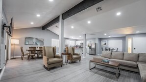 Un vaste espace de vie comprenant un canapé, des fauteuils et une table basse. On y trouve également un coin repas avec une table et des chaises, ainsi qu’une cuisine à l’arrière-plan.