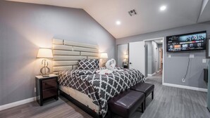 Une chambre moderne avec un grand lit, des tables de chevet, un banc et un téléviseur fixé au mur.
