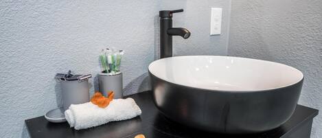A modern bathroom with a large vessel sink, a towel, and toiletries.