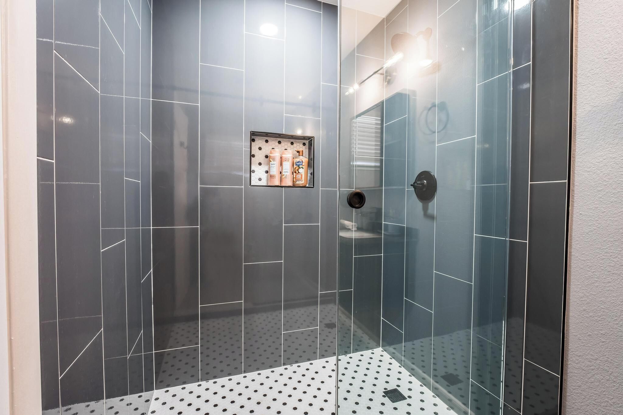 Une douche moderne avec des portes en verre, un sol carrelé et une petite étagère où sont rangés les produits de toilette.