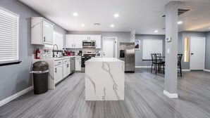 Une cuisine moderne avec des meubles blancs, un îlot central, des appareils en acier inoxydable et un sol gris.