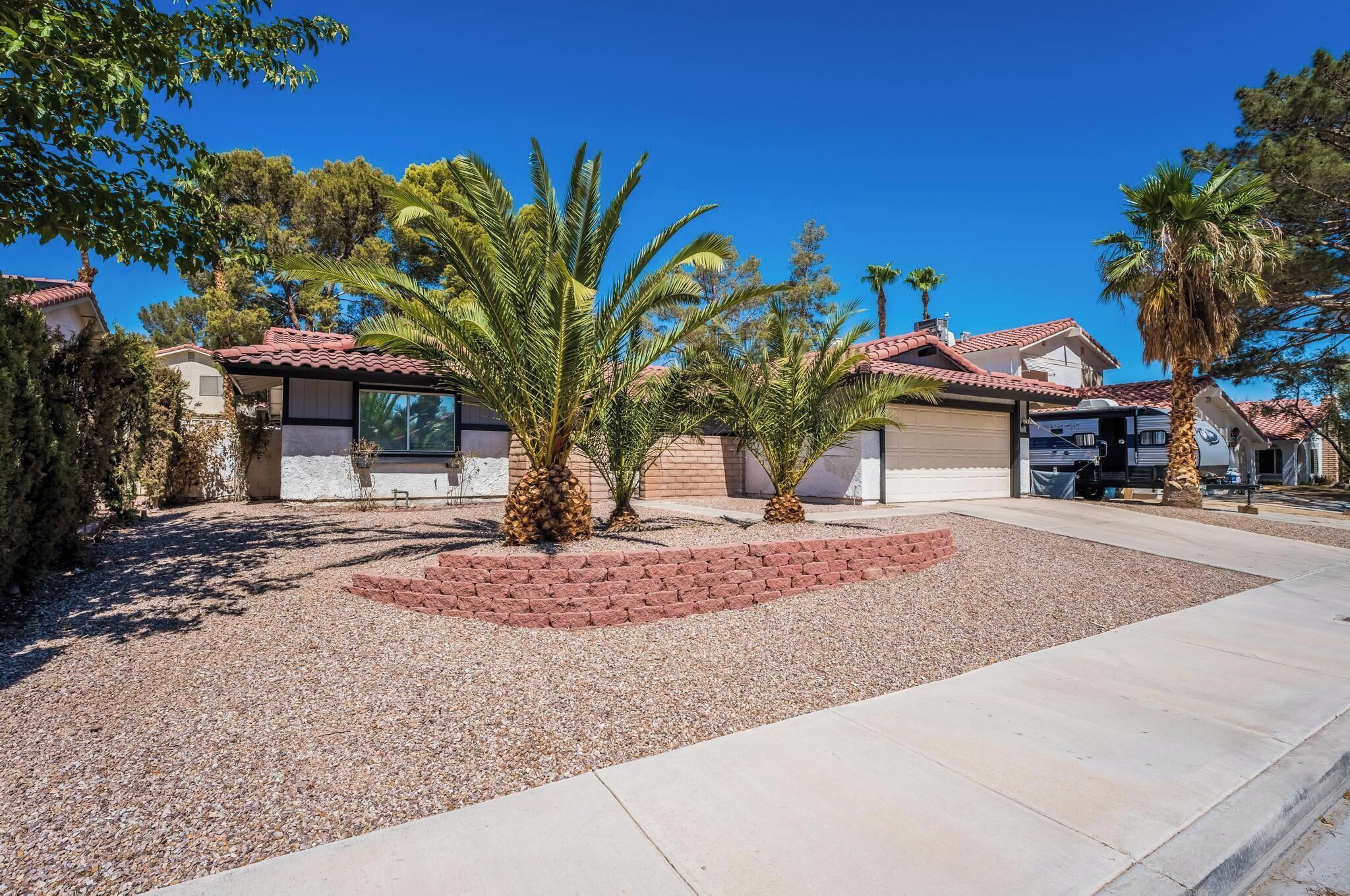 A residential property with a red-tiled roof, a garage, and a landscaped garden with palm trees.