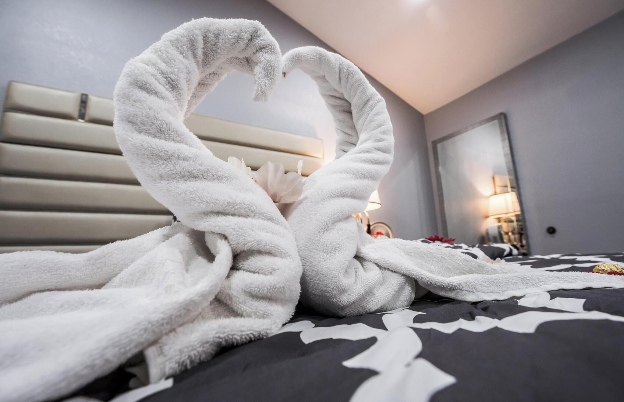 Un lit recouvert d’une couvre-lit à motifs noir et blanc, avec deux serviettes blanches disposées en forme de cœur.