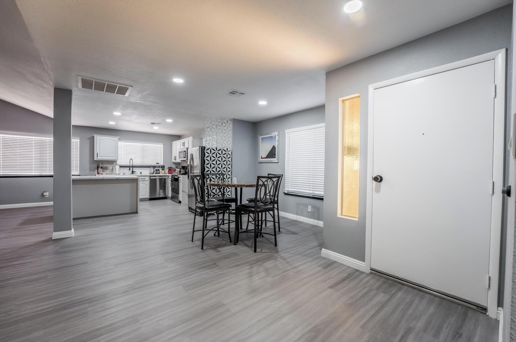 A modern kitchen with a dining area, featuring a central island, dark wooden chairs, and a white door.