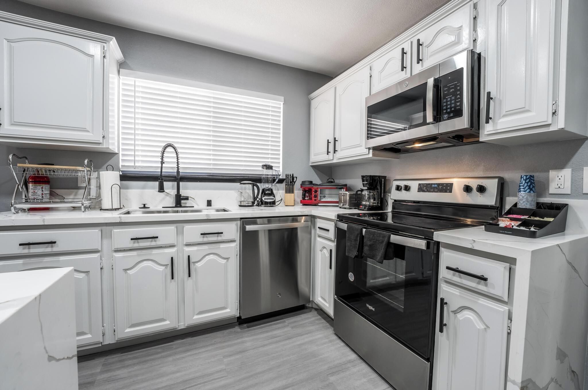 A modern kitchen with white cabinetry, stainless steel appliances, and a window with blinds.