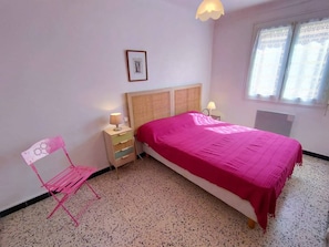 Ein Schlafzimmer mit einem Bett, Nachttischen, einem Sessel, einem Fenster und einem Wandbild.