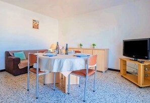 Ein Wohnzimmer mit Esstisch, Stühlen, einer Couch, einem Fernseher und einem Schrank.