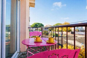 Ein Balkon mit einem rosa Stuhl, einem rosa Tisch und zwei gelben Tassen auf einer Untertasse.