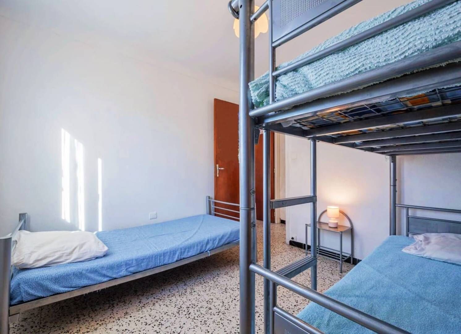 Un dormitorio con literas, una mesa pequeña con una lámpara y una puerta.