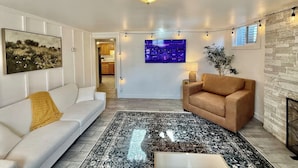Un salon moderne avec un canapé blanc, un canapé marron, un tapis à motifs et un tableau représentant un paysage urbain accroché au mur.